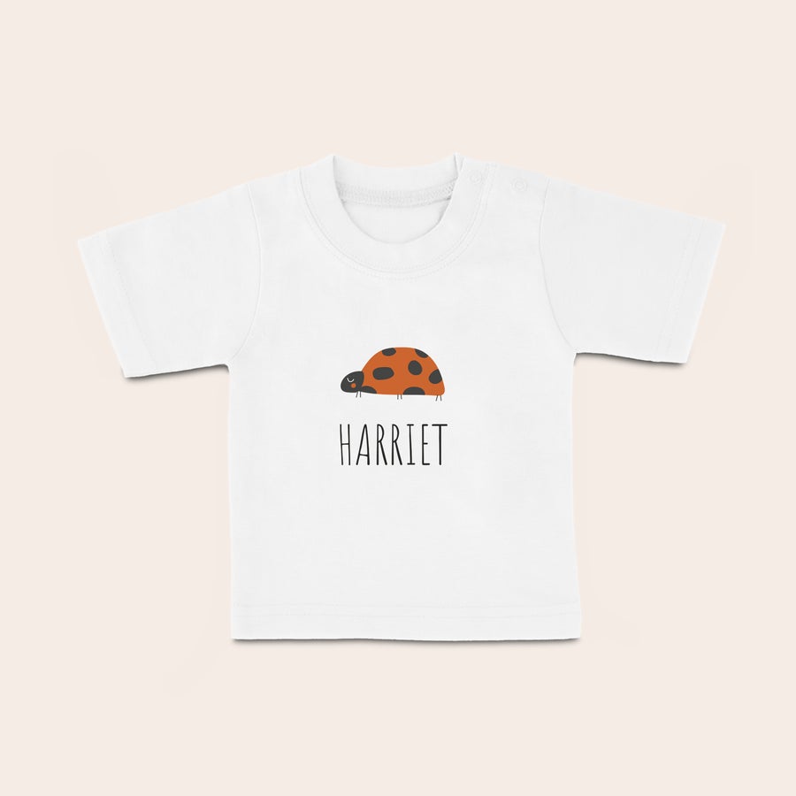 Vlastní dětské tričko Bílé dětské tričko s potiskem, beruškou a jménem Harriet, pro stylové miminko s textem.