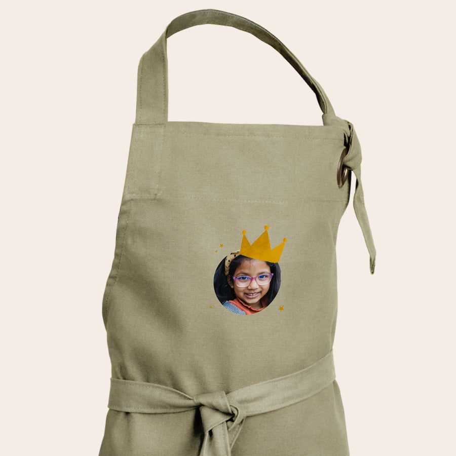Kinderschort met naam Een gepersonaliseerd zandkleurig kinderschort bedrukt met een foto van een meisje met een kroon erop, een persoonlijk schort