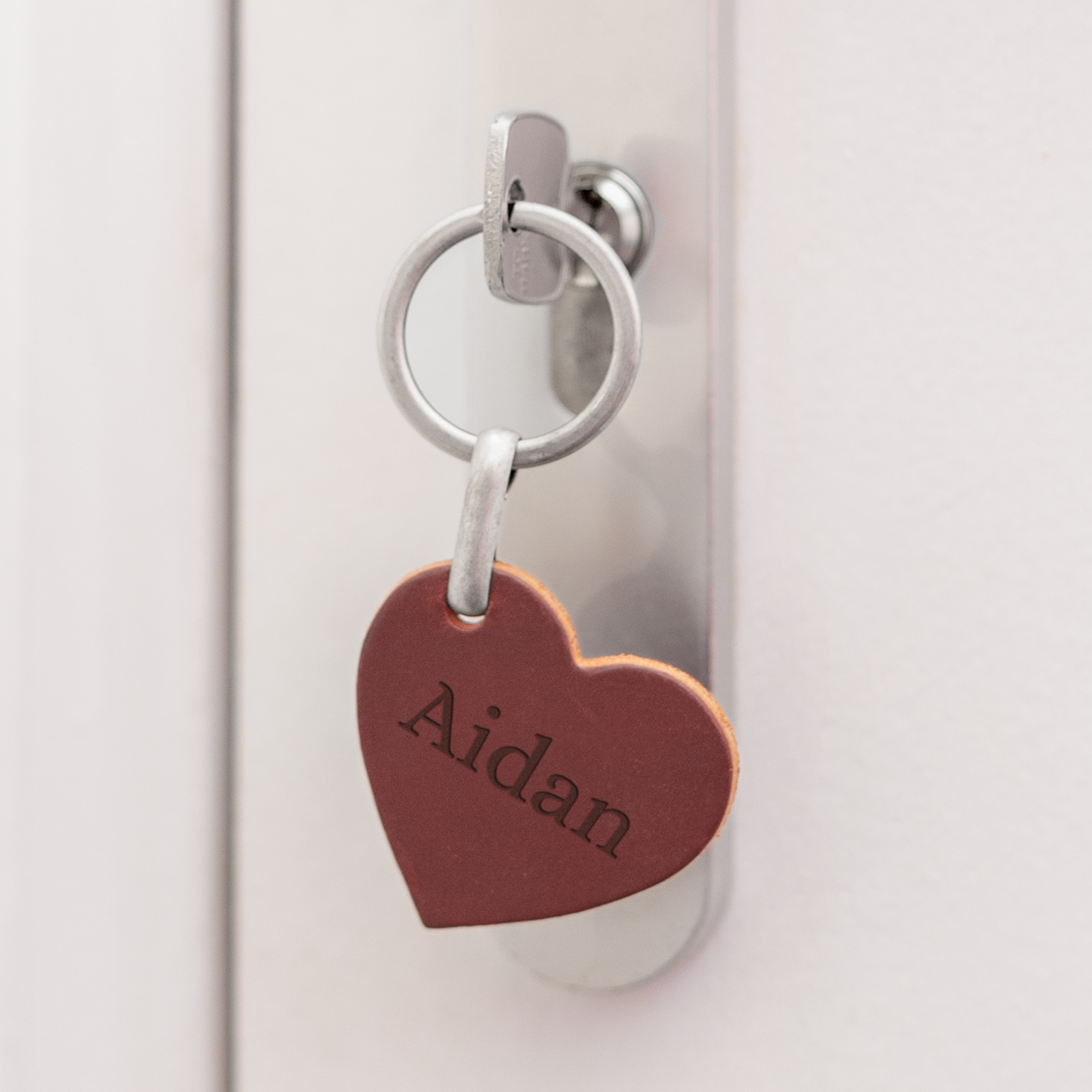 Punainen sydämenmuotoinen nahkainen avaimenperä Aidan-nimen kaiverruksella, roikkuu avaimessa lukossa.