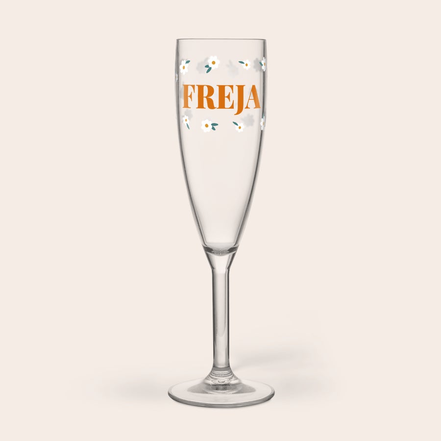 Champagneglas med tryk - Plast Personligt plastglas med namnet FREJA i orange text och vita tusenskönor, tryckt på glaset.