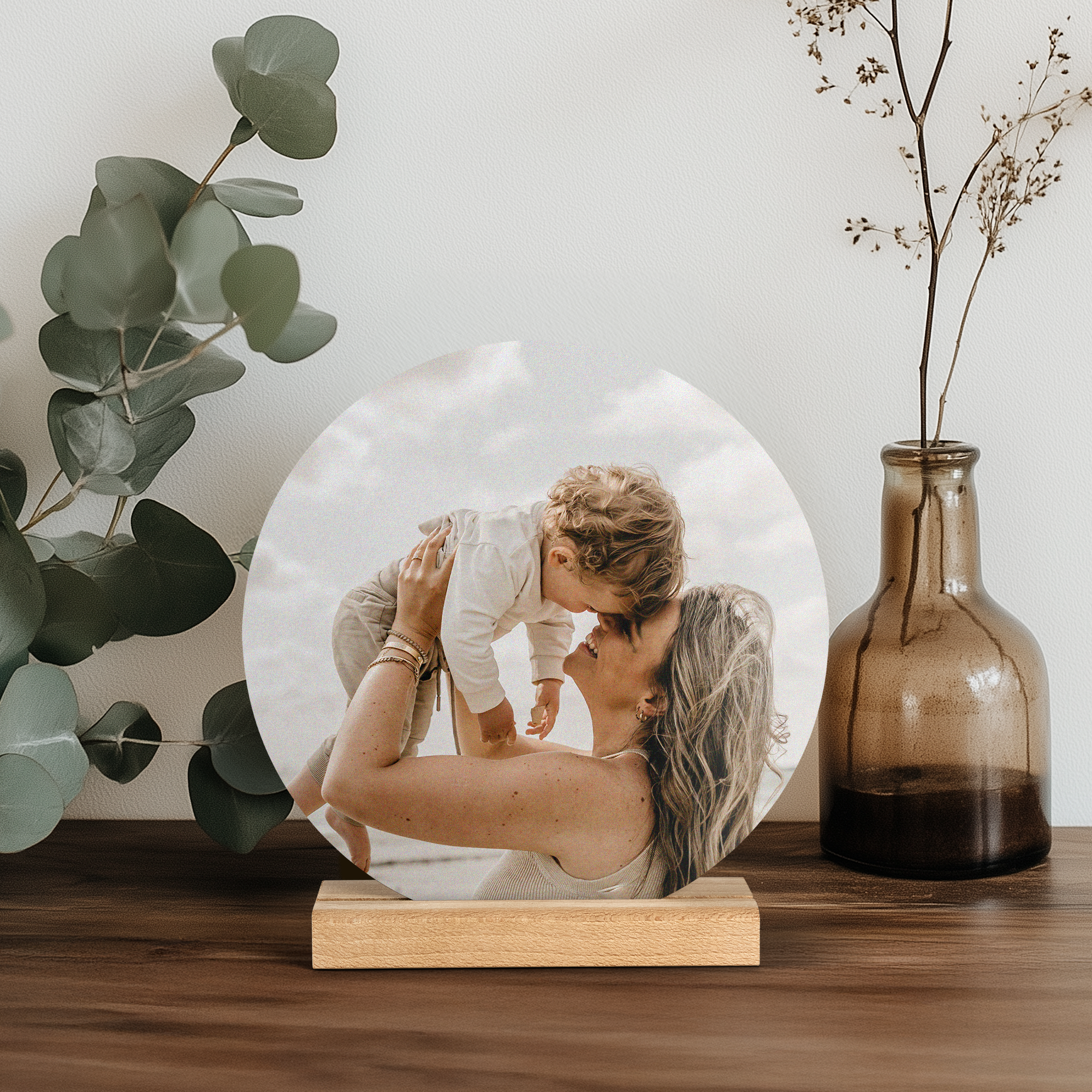 Rund träfotoplatta med ett tryckt foto av en mamma som håller upp sitt barn. Överraska din älskade.