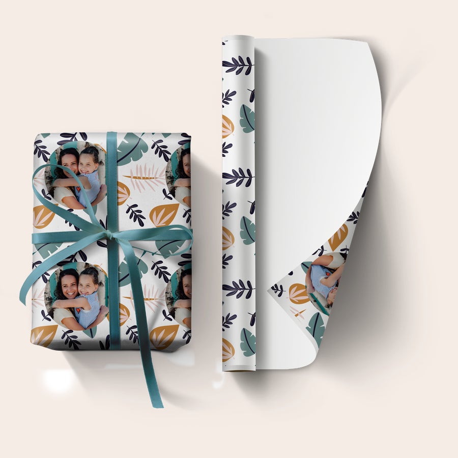 Papel de regalo con foto Envoltorio personalizado con foto de madre e hija sonriendo y motivos de hojas otoñales, enrollado y atado con cinta azul.