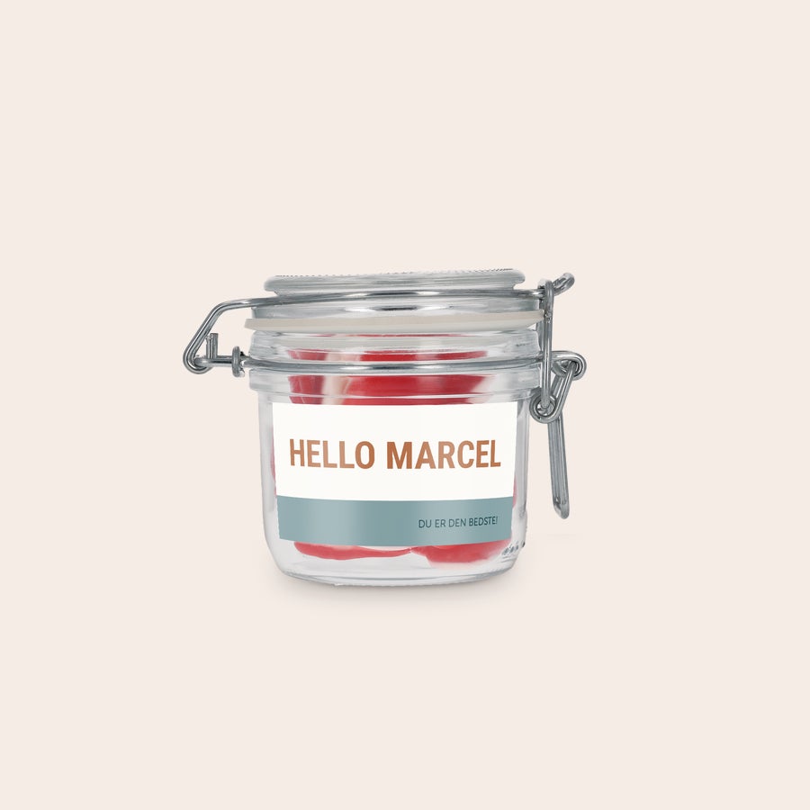 Personlig Glaskrukke med Slik Glaskrukke med hjerteformet slik og personlig etikette. Etiketten er printet med "HELLO MARCEL" og "DU ER DEN BEDSTE!".