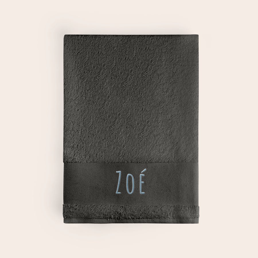 Serviette brodée Serviette gris foncé brodée avec le prénom Zoé en bleu clair. Offrez une superbe serviette brodée avec prénom !