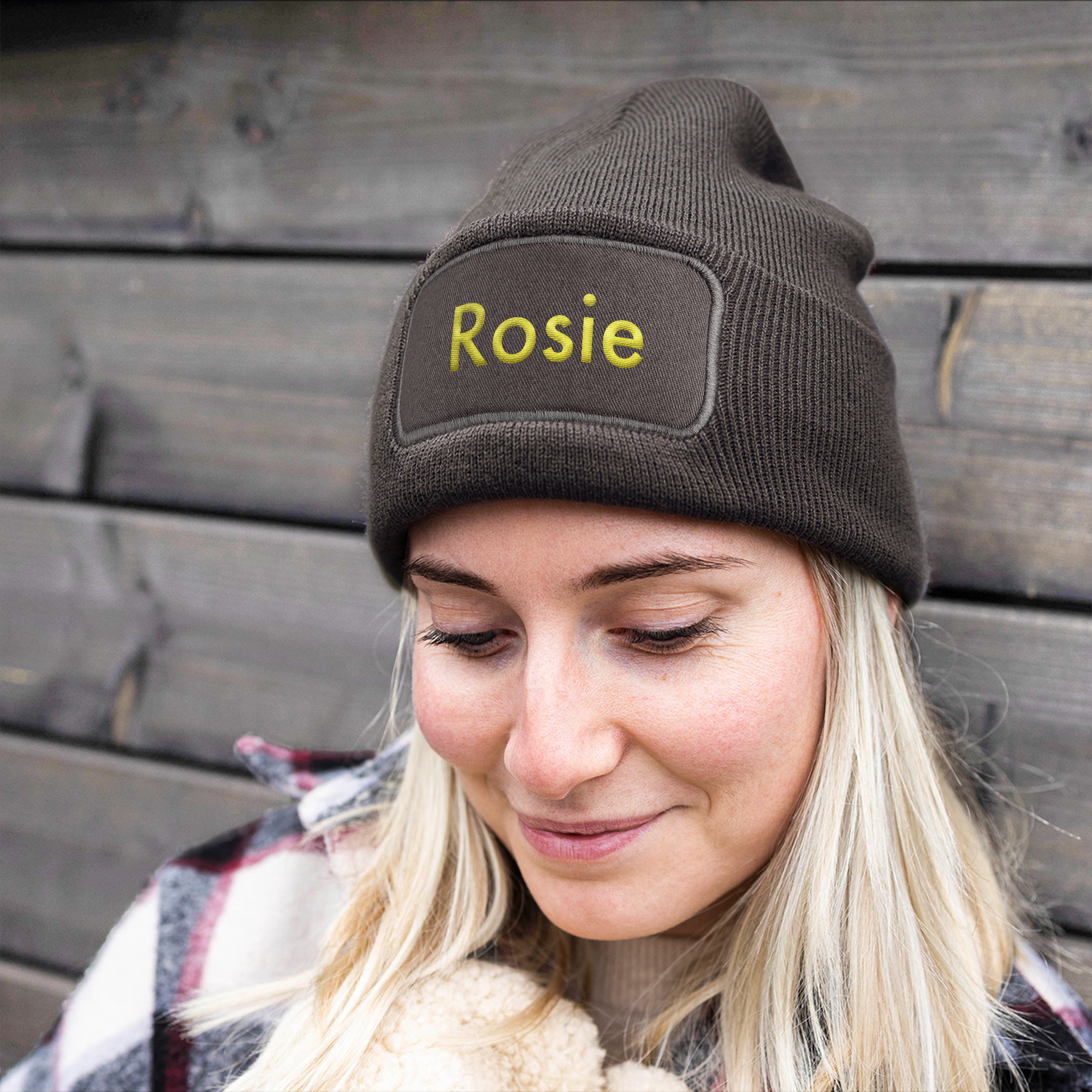 Gorro marrón con el nombre Rosie bordado en amarillo, puesto en una mujer sonriente.