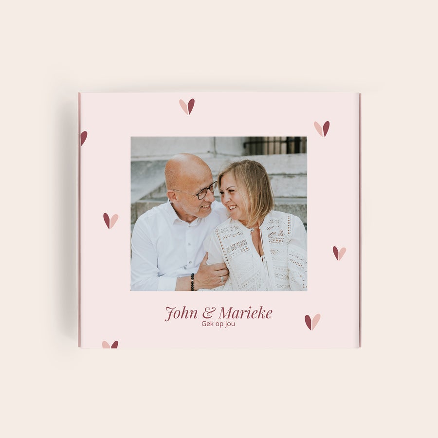 Milka Pralines Love Milka giftbox met foto van John & Marieke en tekst Gek op jou, gedrukt op lichtroze achtergrond met hartjes.