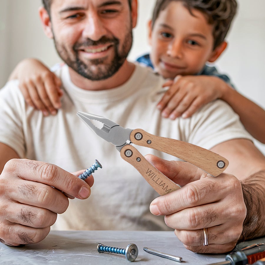 Gravírovaný multitool Personalizovaný multifunkční nástroj s dřevěnými rukojeťmi, vyrytý jménem William, který drží dospělý muž s dítětem v pozadí.