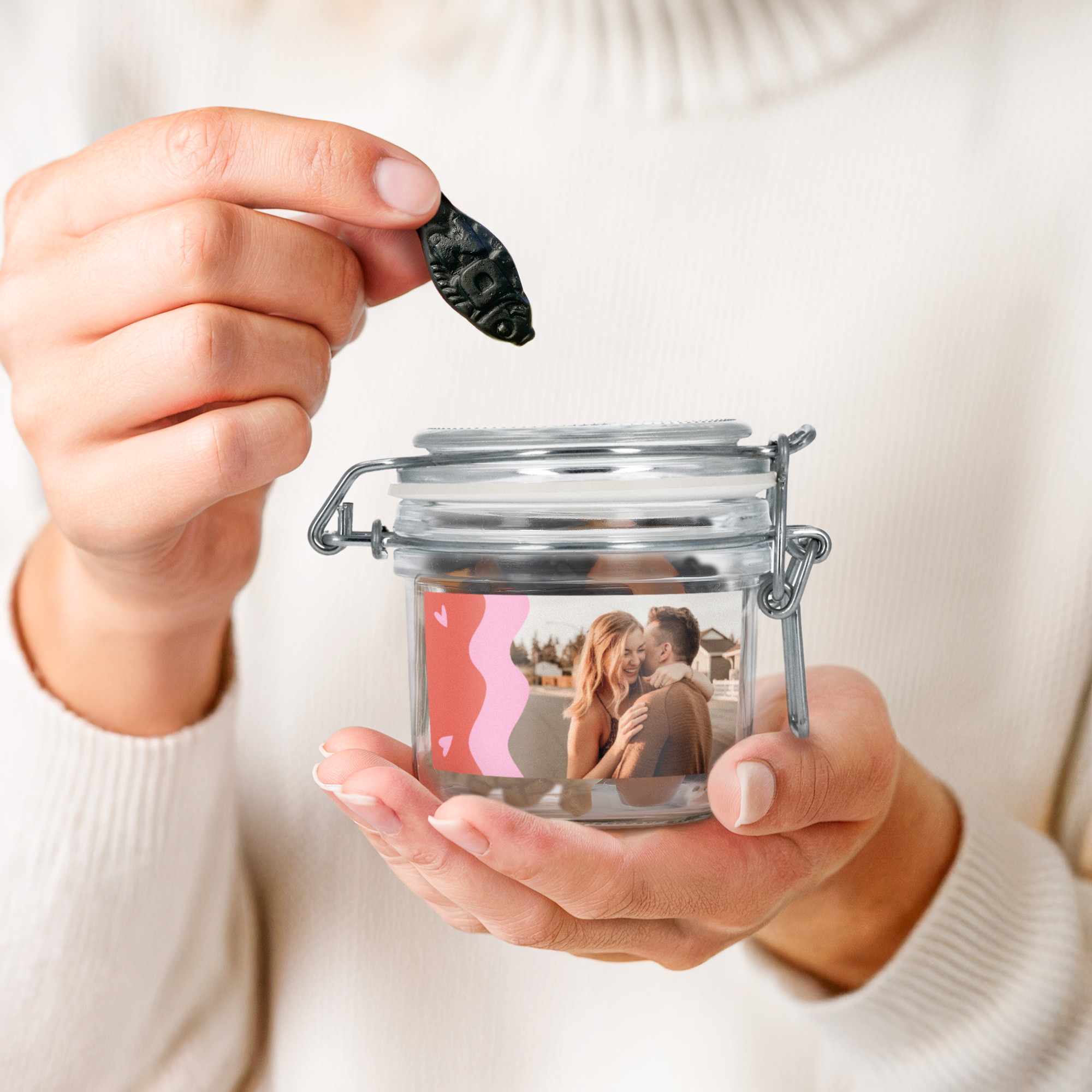 Personalisiertes Bonbonglas mit Lakritzmischung, bedruckt mit einem Pärchenfoto und Herzen, eine Lakritze wird entnommen.