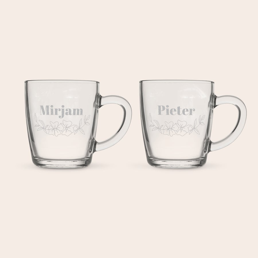 Theeglas graveren Twee blauwe theeglazen, gegraveerd met de namen Mirjam en Pieter en een bloemendesign, ideaal voor theeleuten.