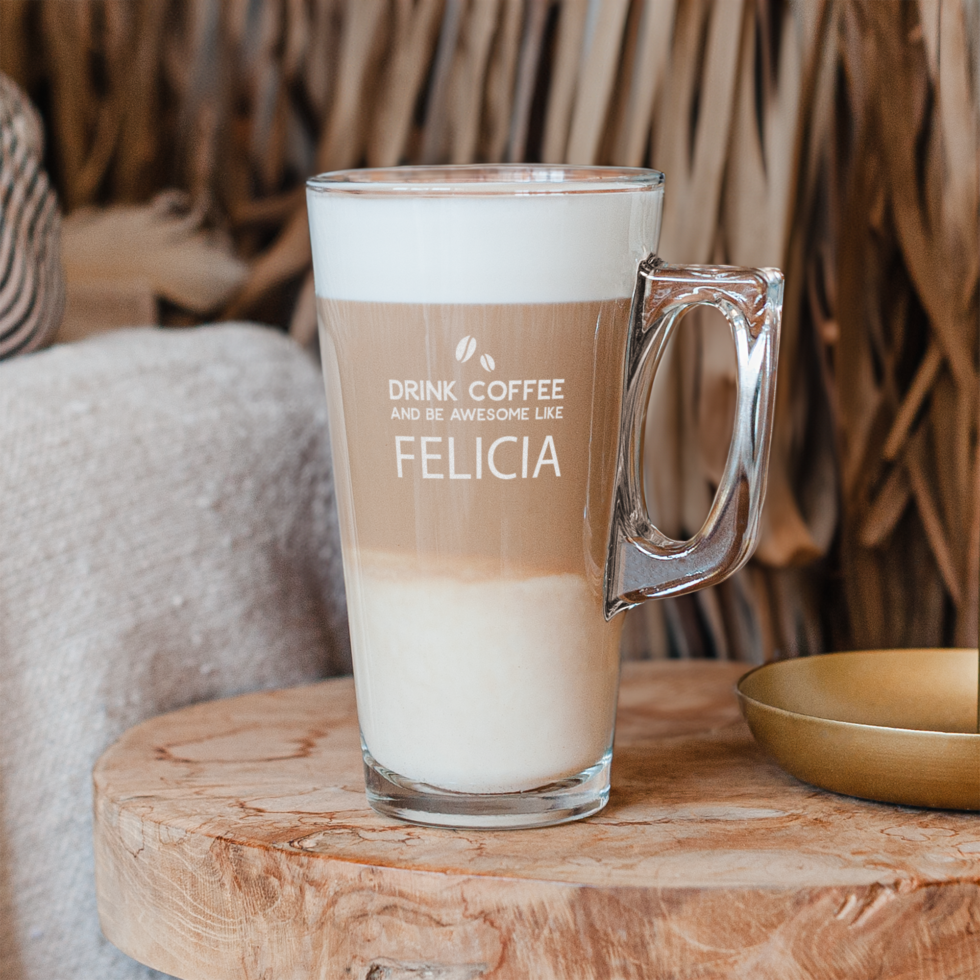 Ett personaliserat latteglas fyllt med latte macchiato, med gravyr av texten "DRINK COFFEE AND BE AWESOME LIKE FELICIA" och två kaffebönor.