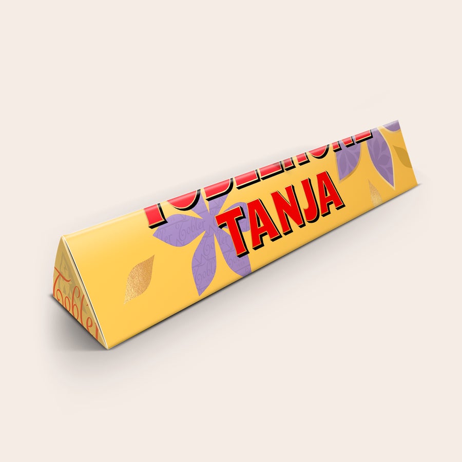 Toblerone med navn - Mors Dag Personlig Toblerone-chokoladebar med navnet TANJA printet på indpakningen og lilla blomster. Overrask din mor med en unik gave.