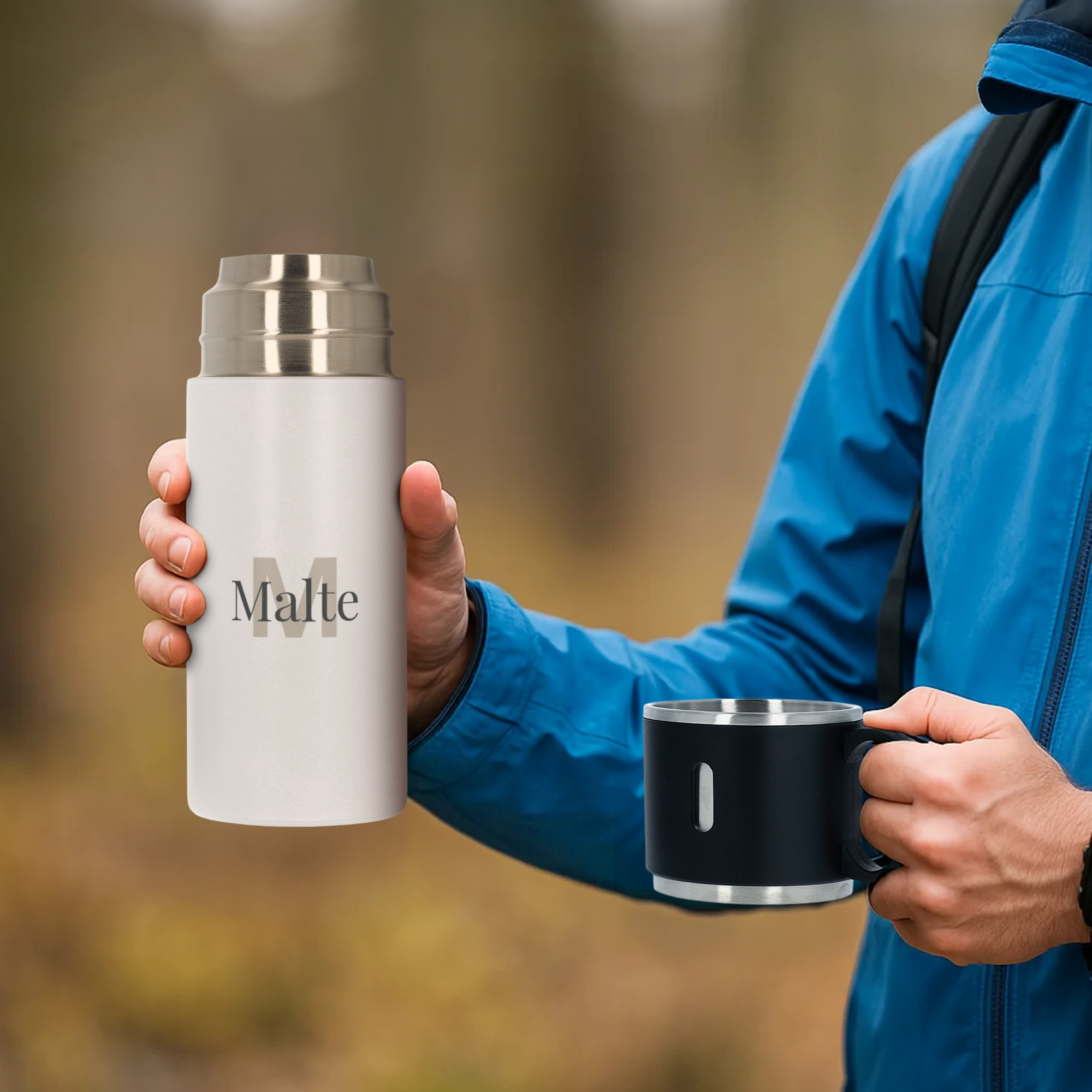 Personlig 350 ml kolv med kopp, vit kolv med tryckt namn Malte, svart kopp i en hand mot en suddig bakgrund av löv. Håll dina drycker precis rätt med en personlig 350 ml kolv med kopp.