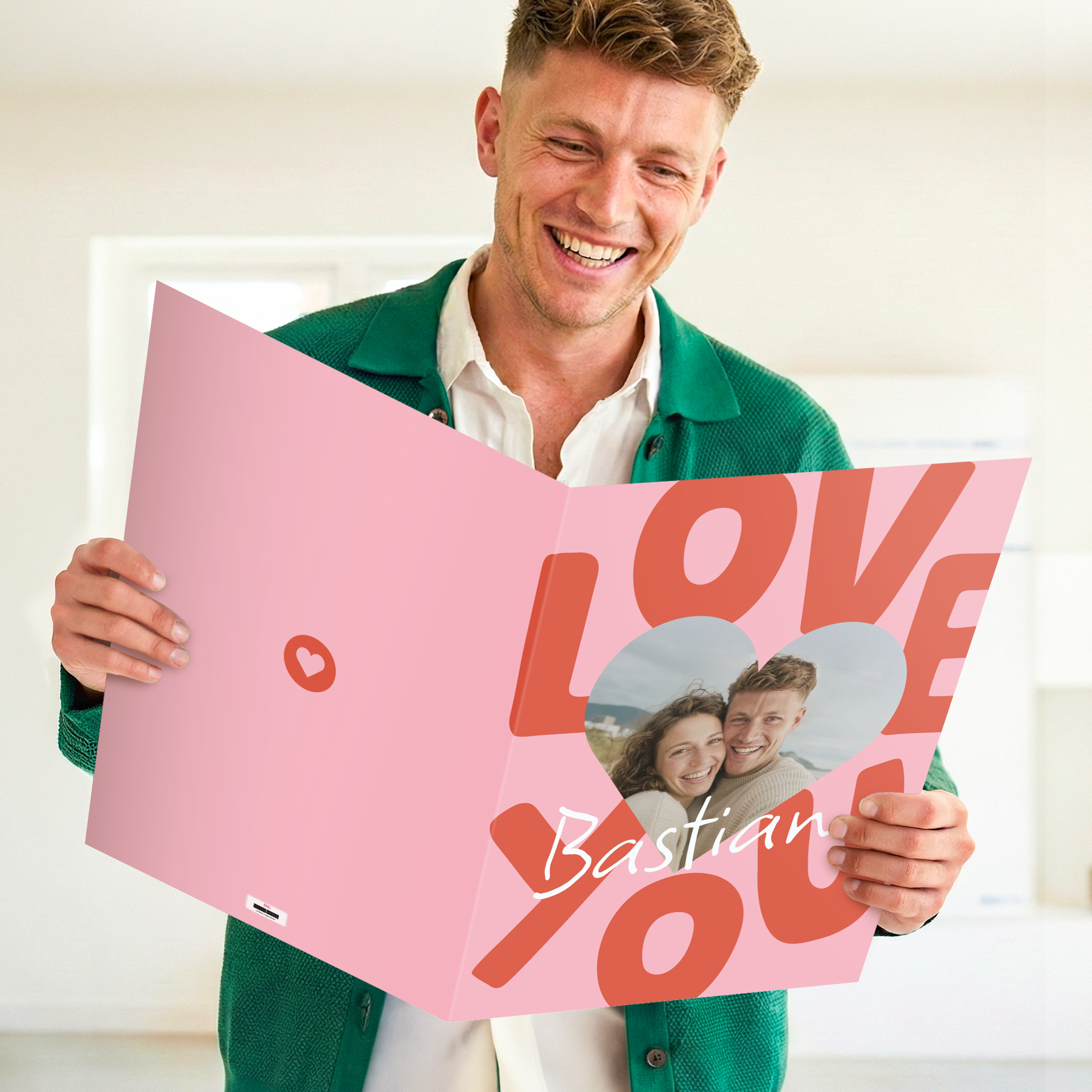 Mann hält eine rosa Personalisierte XXL Karte - 50 cm mit einem gedruckten Foto von einem Paar, dem Text "Love You" und dem Namen "Bastian"