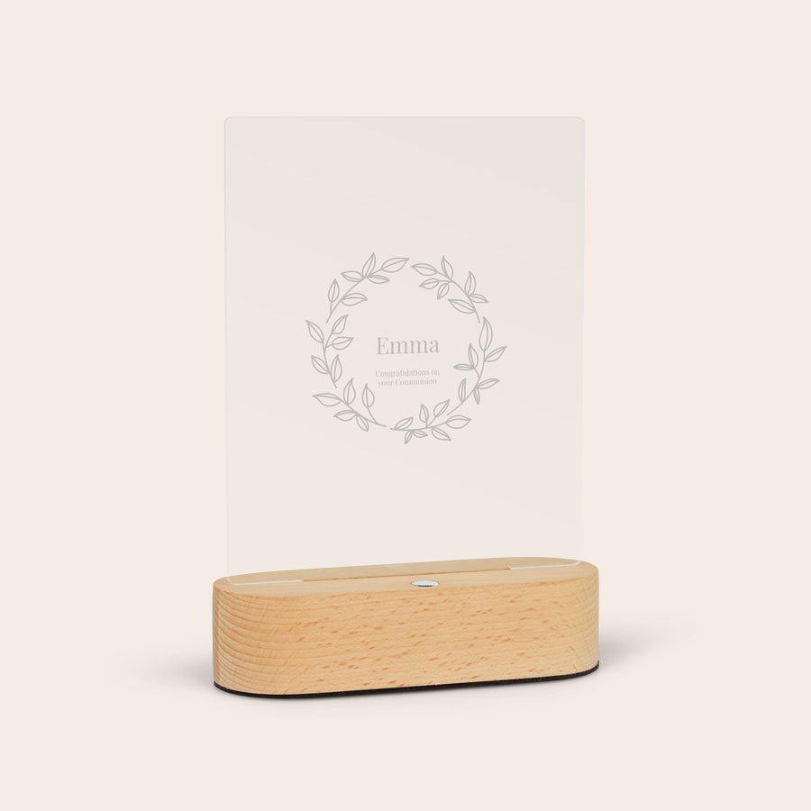 Lumină acrilică cu suport Lumină personalizată acrilică, gravată cu numele Emma și mesajul "Congratulations on your Communion" în interiorul unei ghirlande florale, pe un suport de lemn.