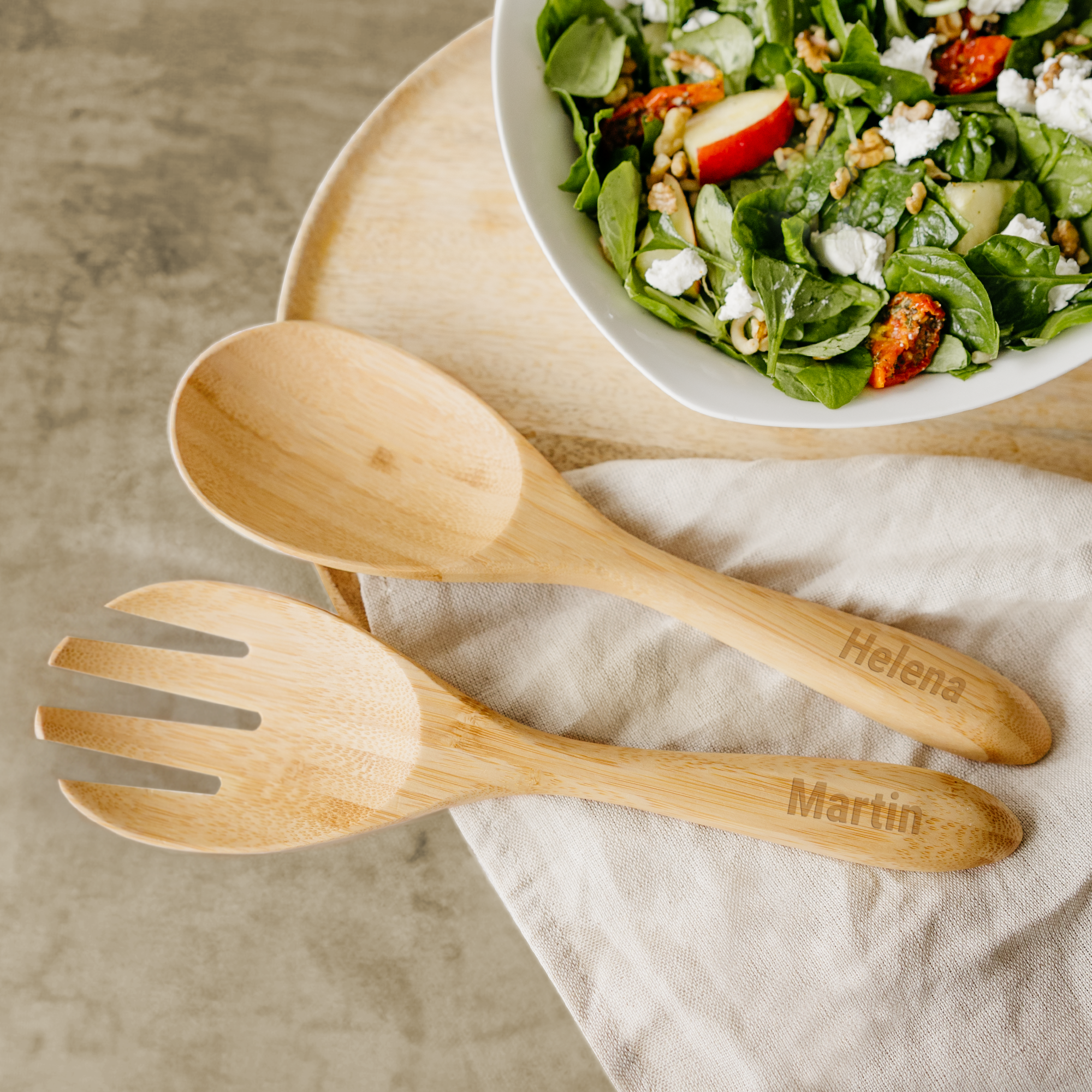 Set de servere pentru salată din bambus, cu nume personalizate "Helena" și "Martin", alături de un bol de salată.