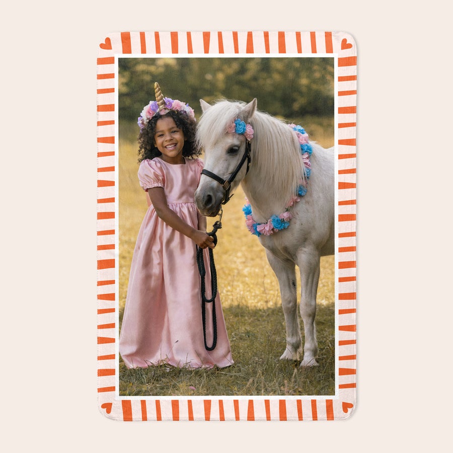 Foto odeja iz flisa Personalizirana odeja iz flisa, tiskana s fotografijo deklice in ponija, obrobljena z oranžnimi črtami.