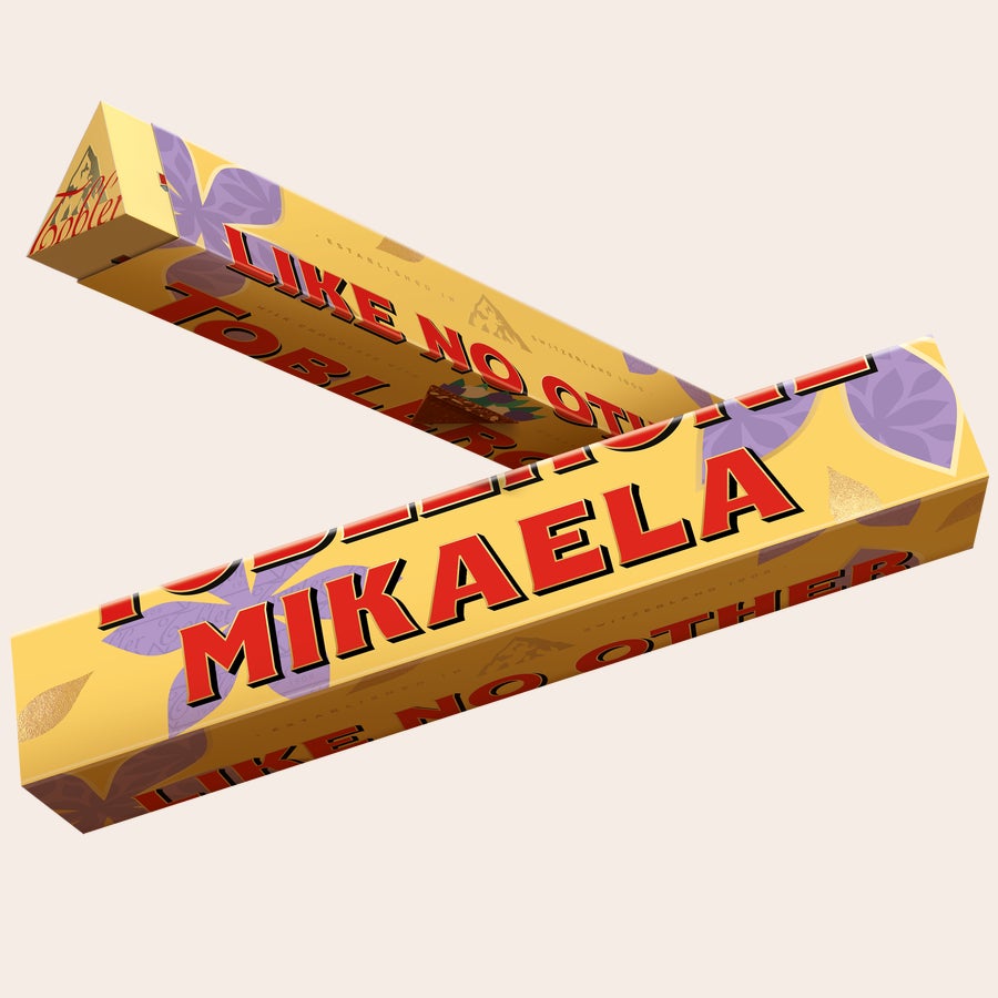 Morsdag Toblerone Personlig Toblerone-chokladkaka med namnet Mikaela tryckt på guldgul förpackning med lila blommor för att överraska din mamma.