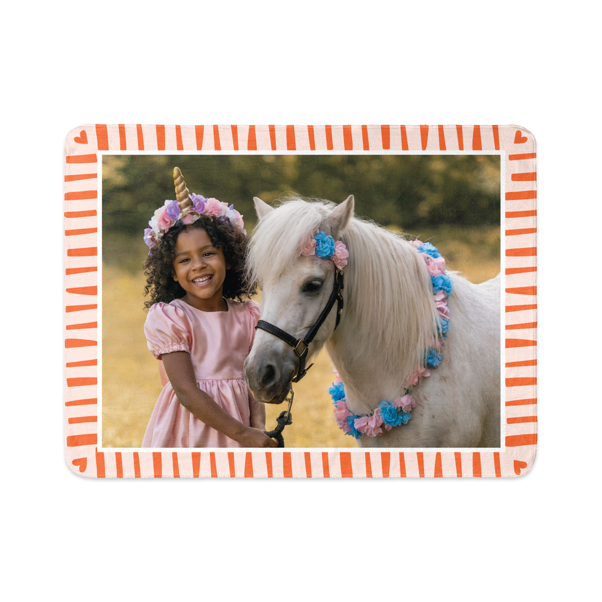 Een fleecedeken bedrukt met foto van een lachend meisje in een eenhoornpak en een wit paard, omlijst met een oranje gestreepte rand en kleine hartjes.