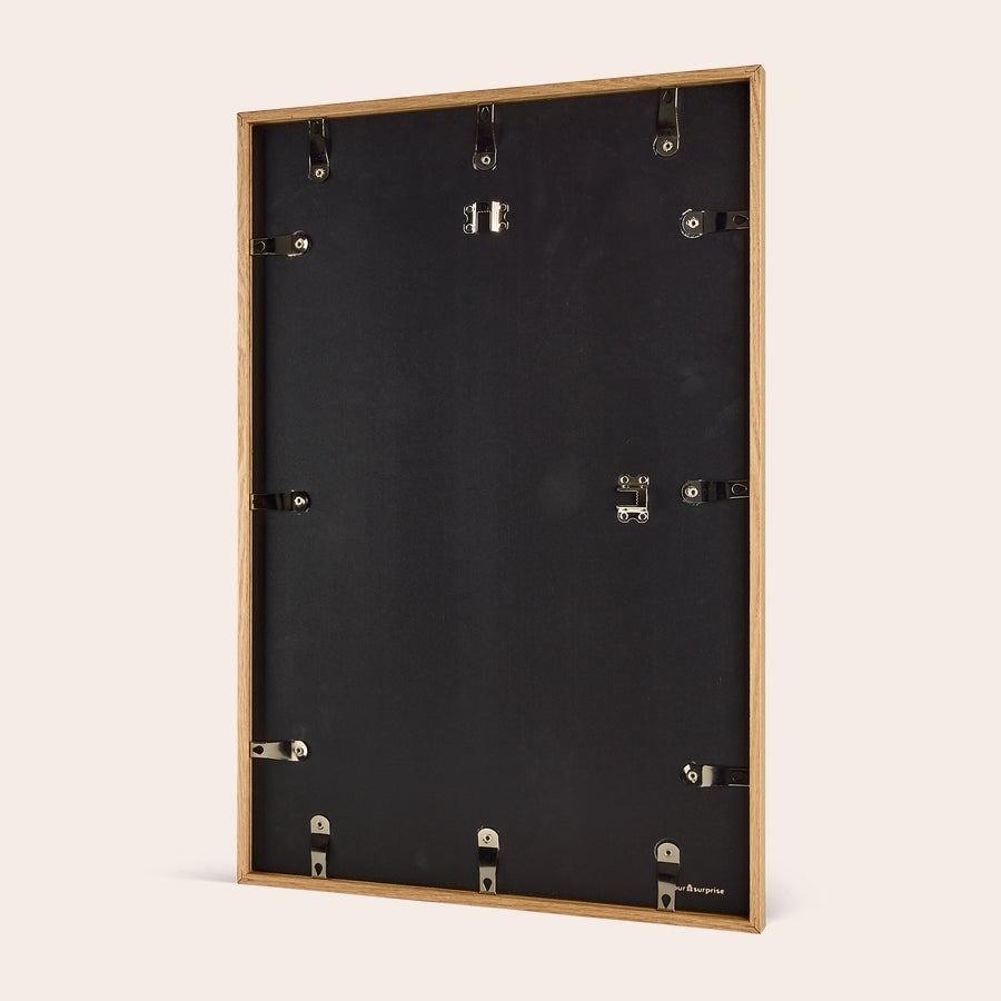 Foto in lijst bestellen Achterkant van een lege, lichtbruine houten fotolijst met metalen ophanghaken en klemmen. Hang jouw mooiste fotomoment aan de muur met deze fotoafdruk inclusief leuke houten lijst.