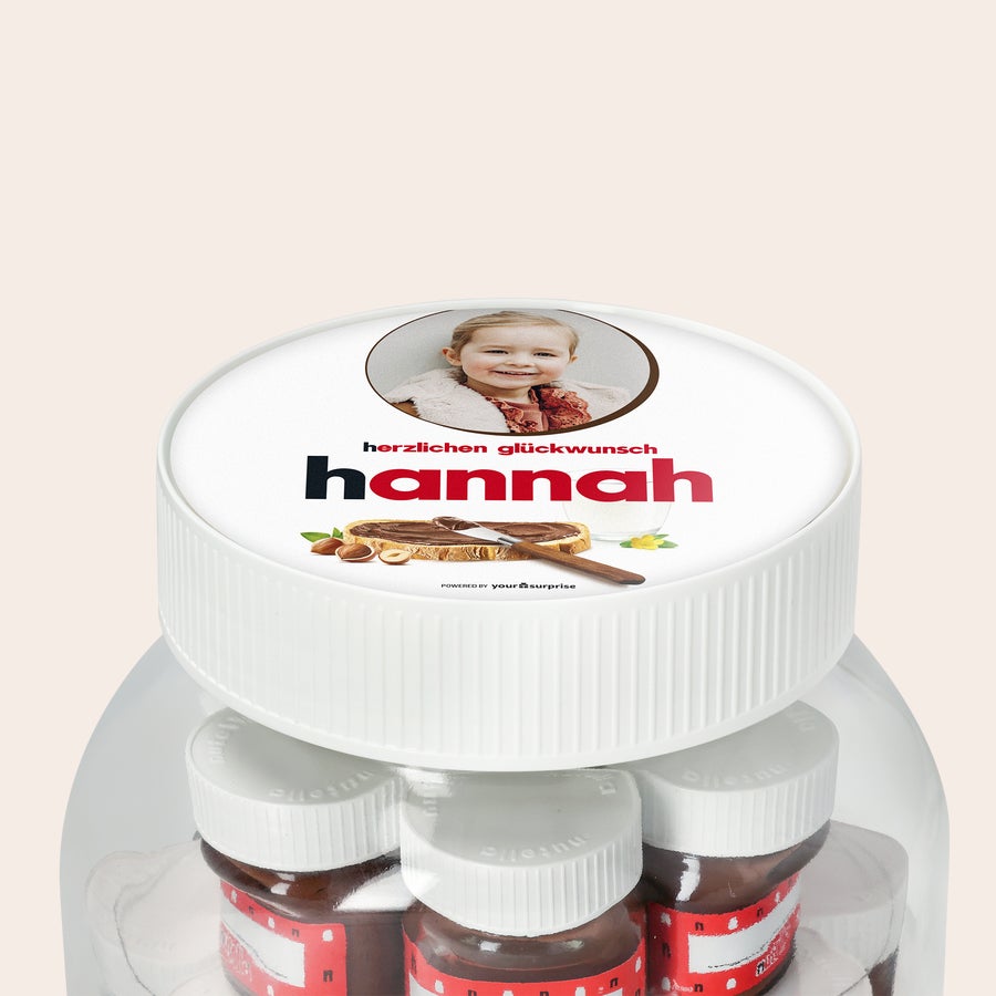 Personalisiertes nutella® Glas XL mit Namen und Foto XL nutella Glas mit Foto von einem lächelnden Mädchen, dem Namen Hannah und Glückwünschen, darüber sind kleine nutella Gläser zu sehen.