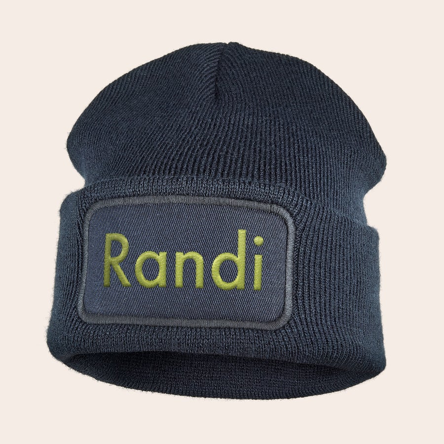 Broderte lue Mørkeblå beanie med "Randi" brodert i gult på en lapp, perfekt for å holde ørene varme.