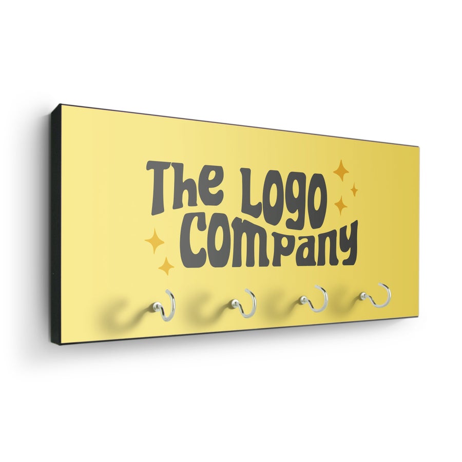 Gul nyckelhylla med fyra krokar, texten "The Logo Company" tryckt i svart och små stjärnor. En personlig nyckelrad för att aldrig tappa bort nycklarna.