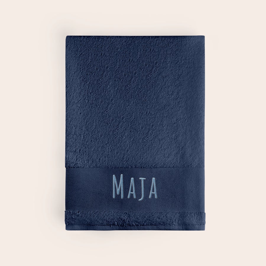 Badehåndkle med tekst Personlig, marineblått badehåndkle brodert med navnet MAJA i lyseblått. Skap noe unikt.