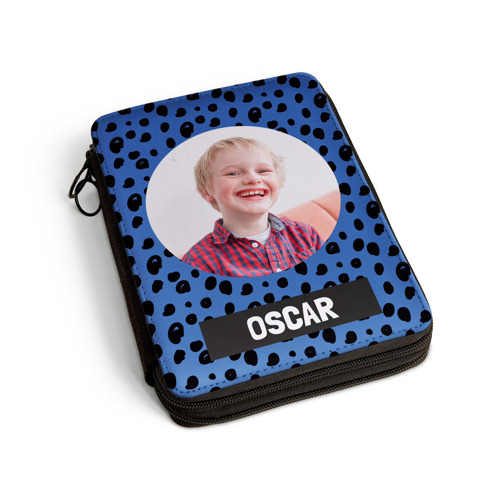 Mit der fröhlich bedruckten Federmappe 2 Fach, personalisiert mit einem Foto eines lachenden Jungen und dem Namen "OSCAR" auf blauer Grundfarbe mit schwarzen Tupfen.