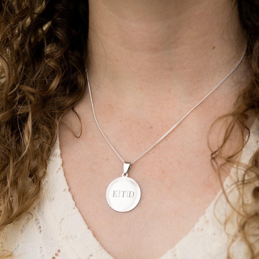 Round pendant necklace Silver round personalized engraved pendant with initials E T D worn on a chain by a woman.