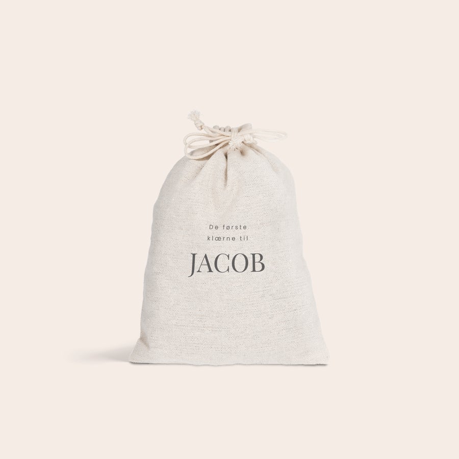 Gavepose med løpesnor Personlig snorpose i bomull, trykket med teksten "De første klærne til JACOB".