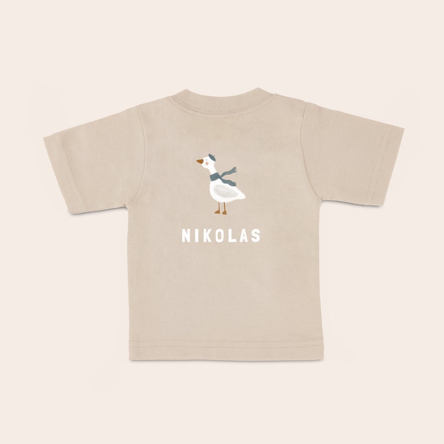Baby t shirt bedrucken Beiges Baby T-Shirt mit Aufdruck einer Gans, die einen blauen Schal und Hut trägt, und dem Namen NIKOLAS personalisiert.