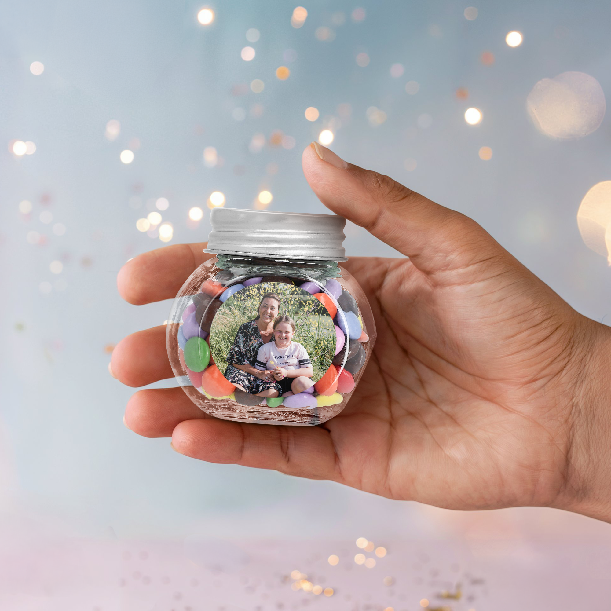 Hand holding a personalized glass jar favour filled with colourful chocolates and printed with a photo of a woman and child.