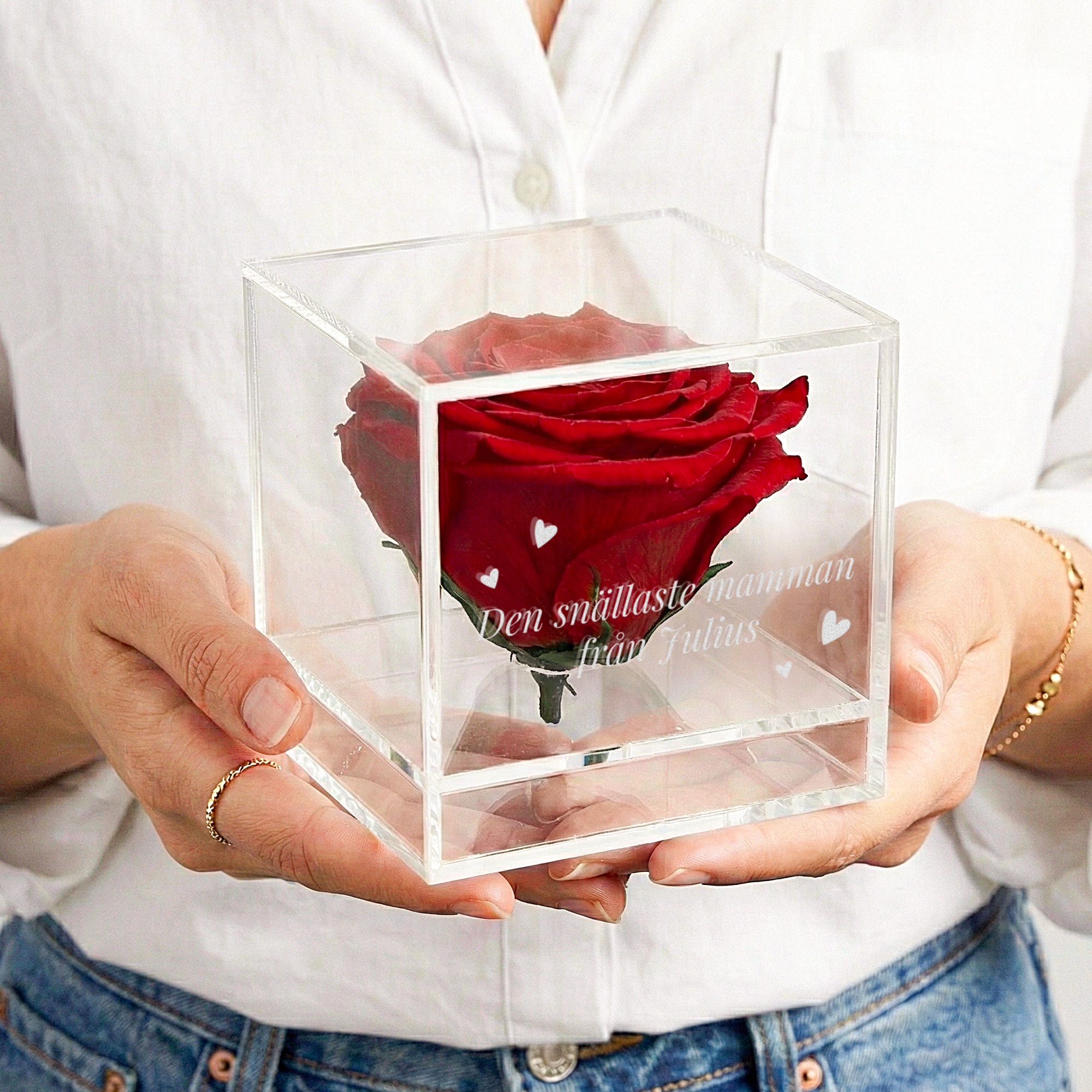 Evig ros i graverat plexiglasfodral med personlig text Den snällaste mamman från Julius och hjärtan, hållen av händer i en vit skjorta.